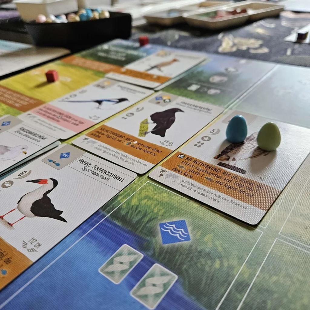 Ein Spieler-Tableau von Flügelschlag mit Vogelkarten und Miniatur-Eiern.